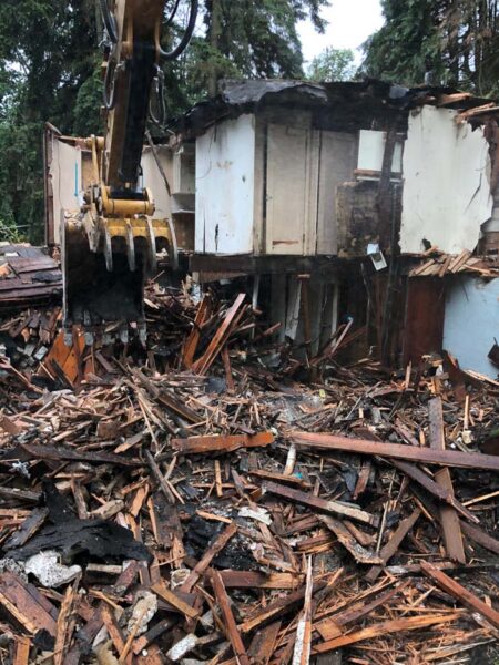 Excavator demolishing a wooden house among debris